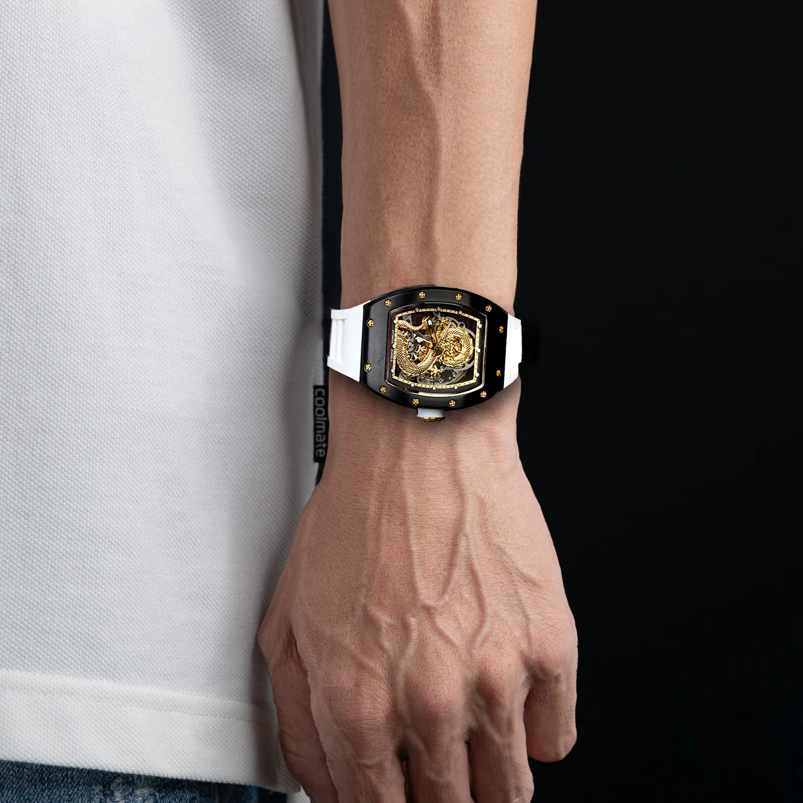Close-up of a wrist wearing a gold and black watch with a white shirt and blue jeans.